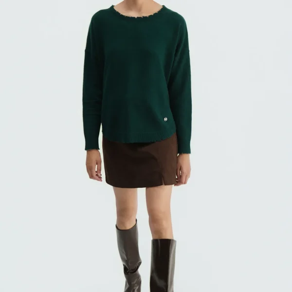 Jersey oversize deshilachado verde oscuro BSB, de frente con minifalda y botas Jersey oversize deshilachado verde oscuro BSB, de frente con minifalda y botas