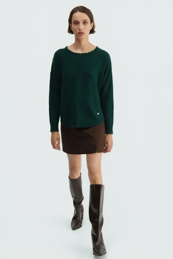 Jersey oversize deshilachado verde oscuro BSB, de frente con minifalda y botas Jersey oversize deshilachado verde oscuro BSB, de frente con minifalda y botas