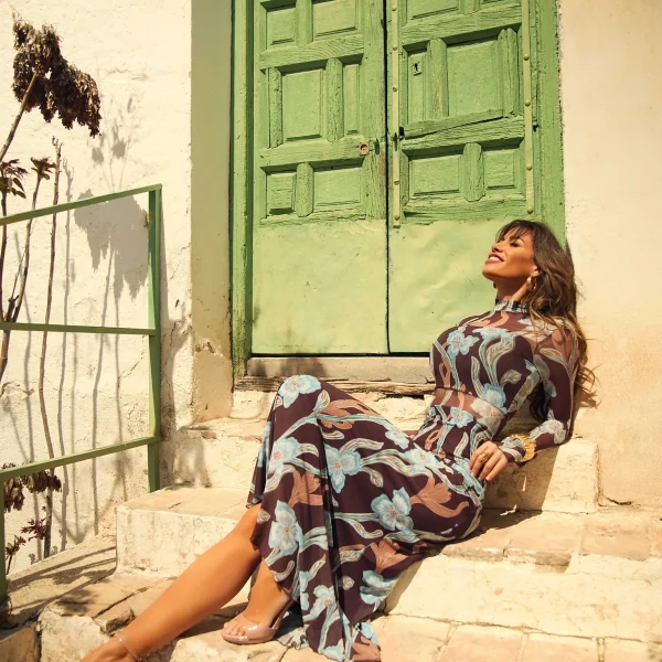 Vestido Breka de Camaleónica, estampado floral malva y azul, sentada en el exterior de una casa mediterránea.