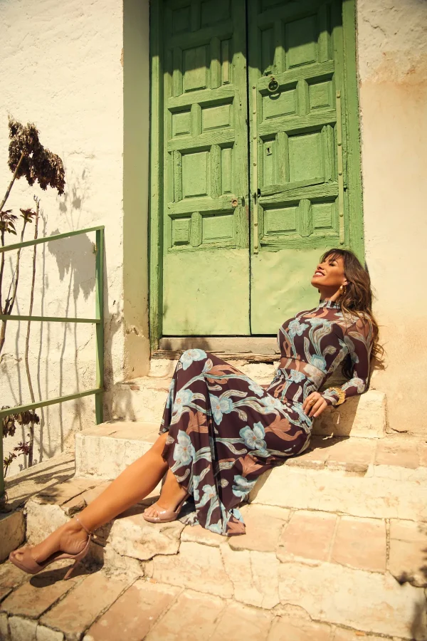 Vestido Breka de Camaleónica, estampado floral malva y azul, sentada en el exterior de una casa mediterránea.