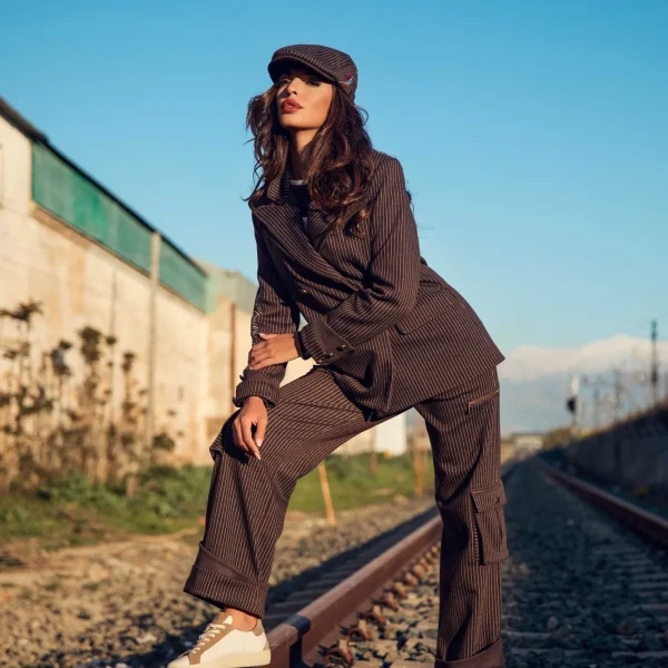 camaleonica-boina-elkorn-blazer-jasper-pantalon-haldor-lateral-2 Boina Elkorn, blazer Jasper y pantalón Haldor Camaleónica de raya diplomática marrón con bajo vuelto, vistos de lado en las vías