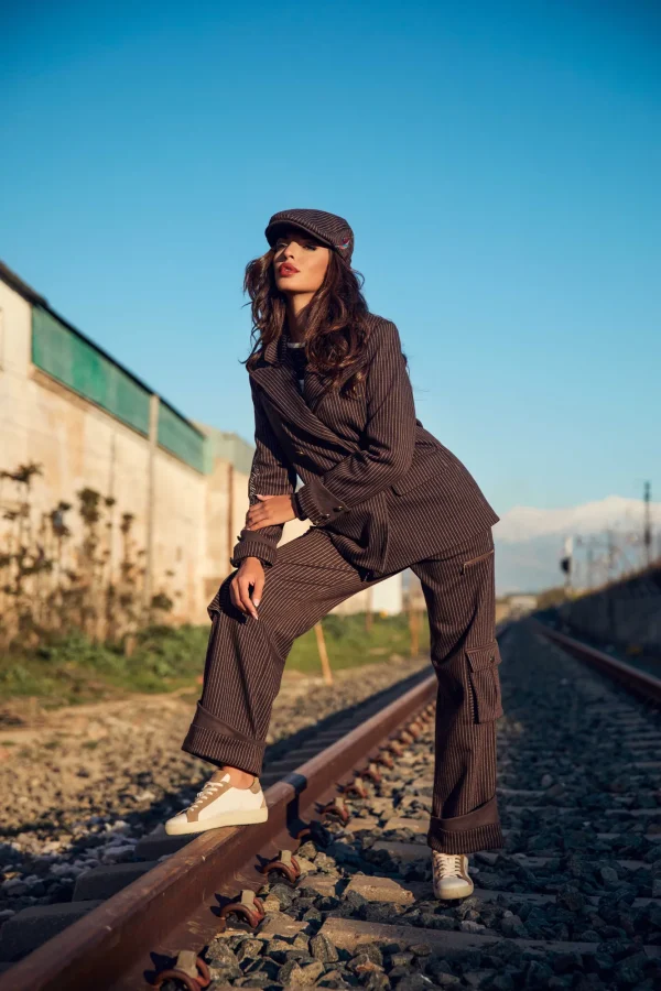 camaleonica-boina-elkorn-blazer-jasper-pantalon-haldor-lateral-2 Boina Elkorn, blazer Jasper y pantalón Haldor Camaleónica de raya diplomática marrón con bajo vuelto, vistos de lado en las vías